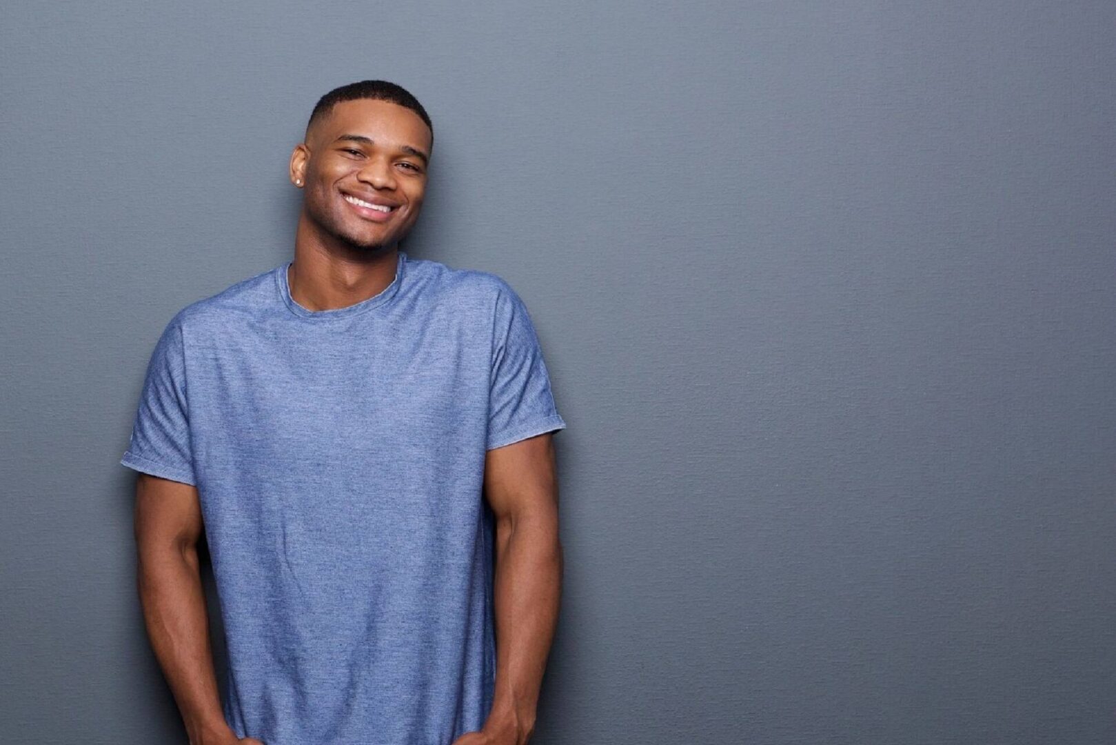 Smiling young man in a blue t-shirt against a gray background.
