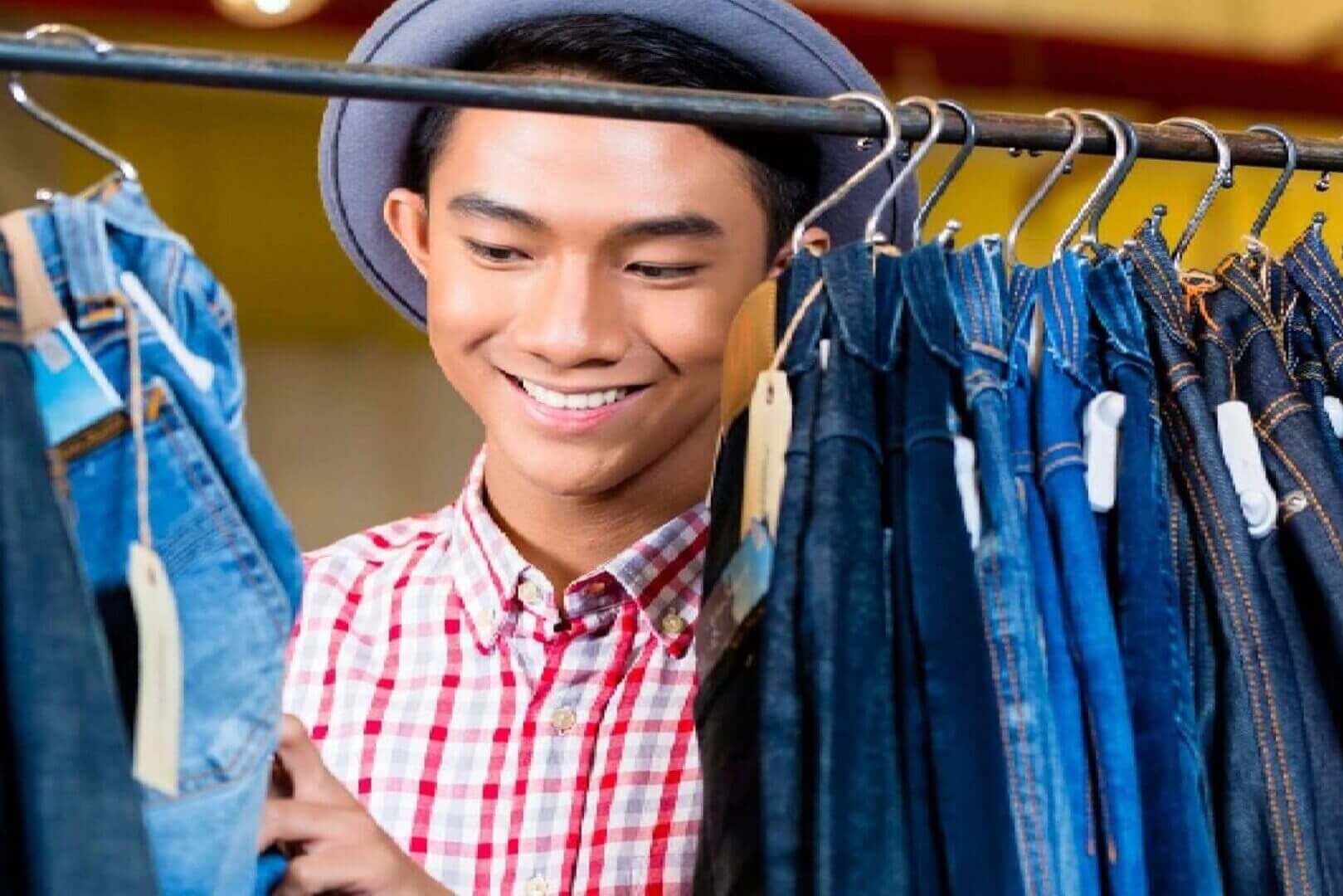 A young man smiling while shopping for jeans in a store.